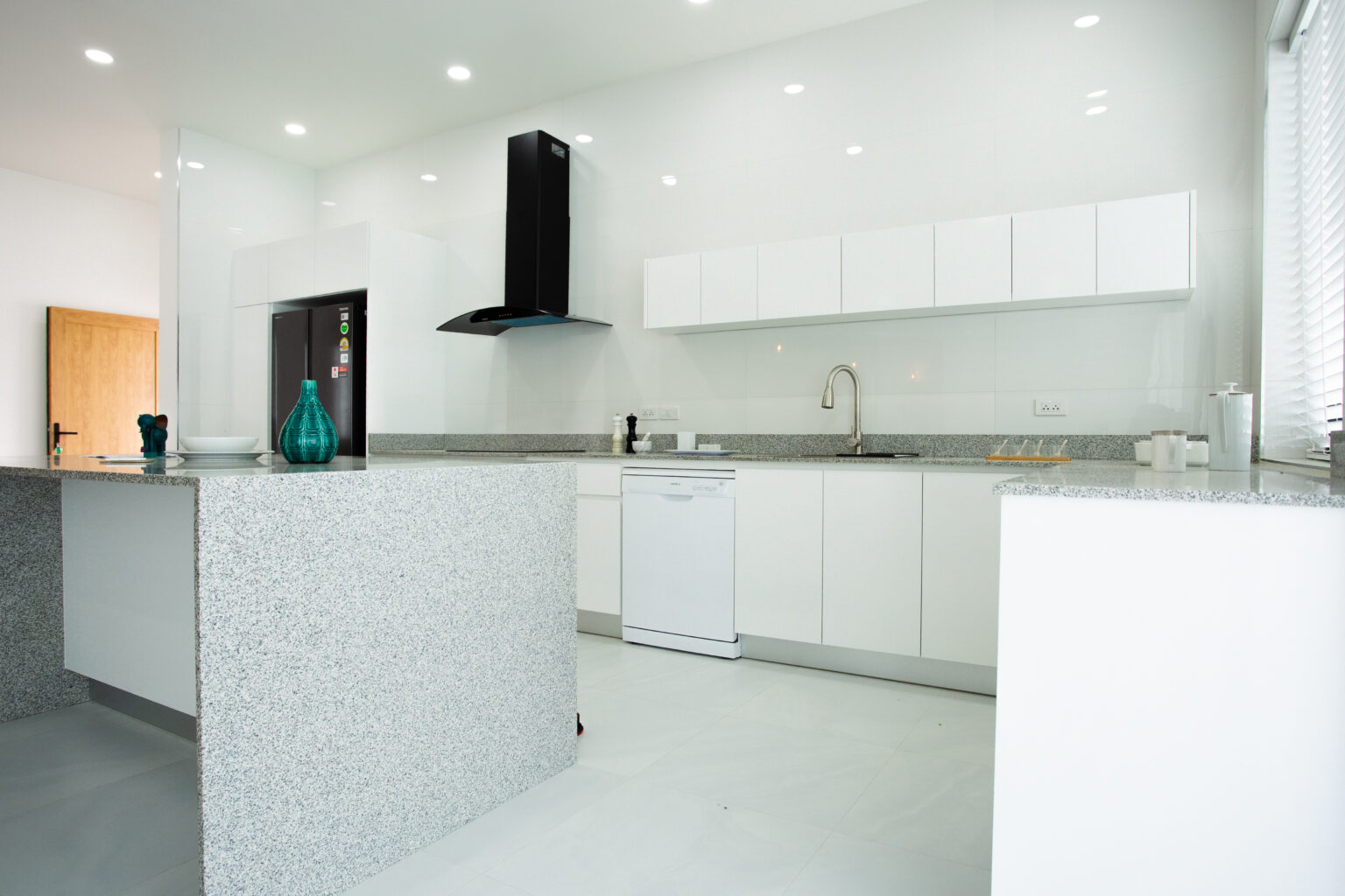 Modern white kitchen with built-in cabinets, black range hood, and a sleek island counter in a bright open space.
