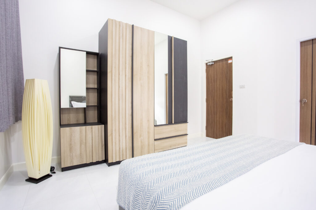 A bright bedroom corner at Villa de L’Amitié Huahin featuring a light wood wardrobe with a full-length mirror, a minimalist floor lamp, and clean white walls.