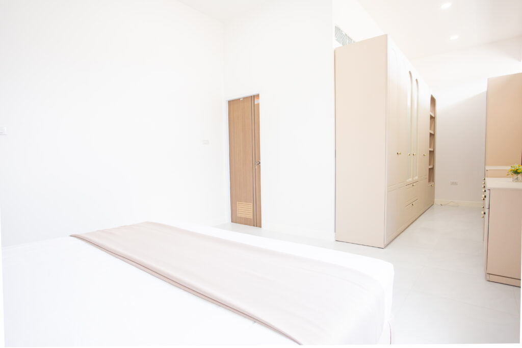 A bright and minimalist bedroom layout at Villa de L’Amitié Huahin featuring a king-sized bed with neutral linens and a spacious built-in wardrobe area.